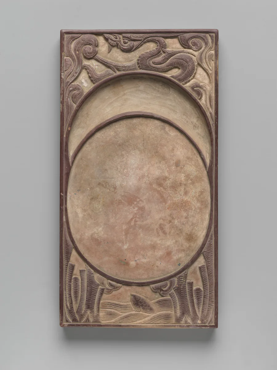 A rectangular inkstone with a round grinding well; a dragon coils above it and a carp rises below.